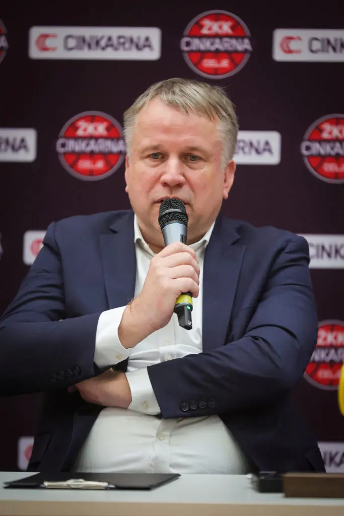 Govorec v modri obleki z mikrofonom na novinarski konferenci.