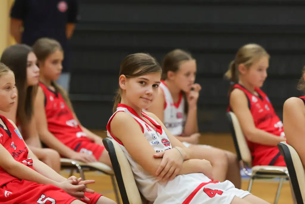 Mlade košarkarice v klubskih dresih med spremljanjem dogodka.